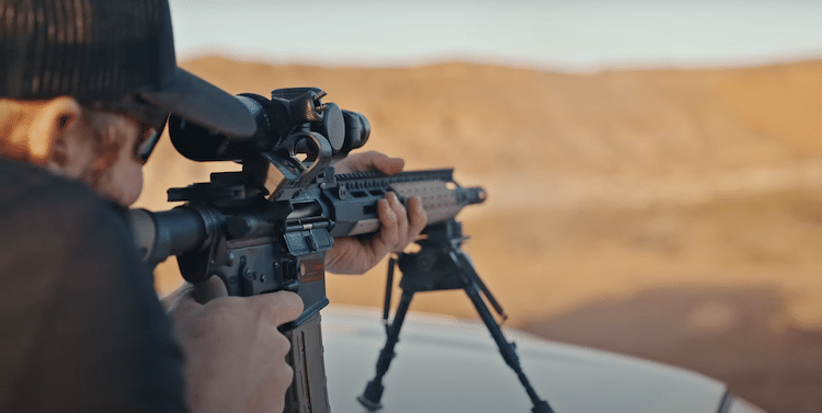Man aiming a rifle with a mounted scope