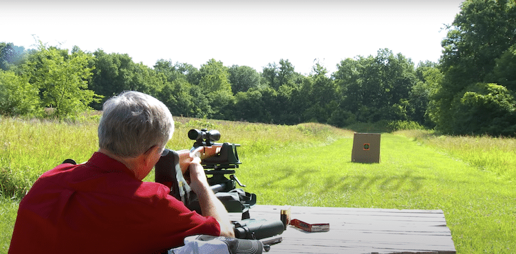 Man looking through a long eye relief scope on a grassy field