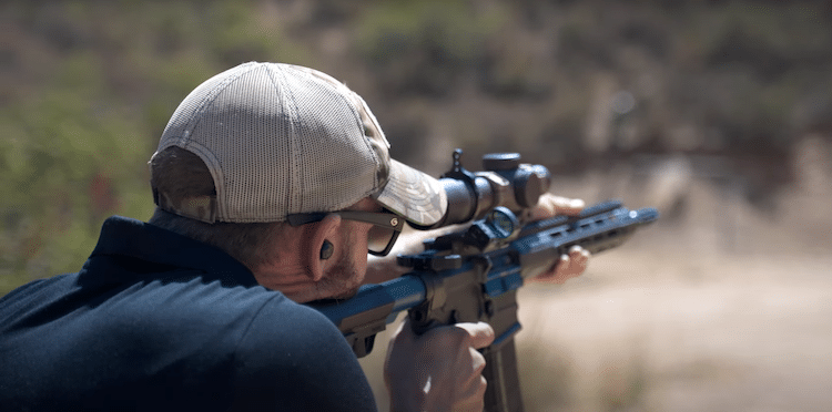 Image of a man holding a rifle with a red dot scope