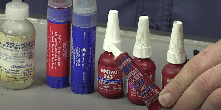 Image of a hand holding a blue threadlocker and different types of threadlocker in the background