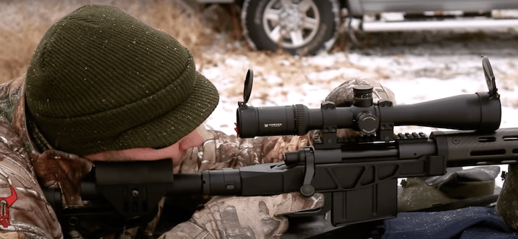 Man looking through a scope mounted on a rifle