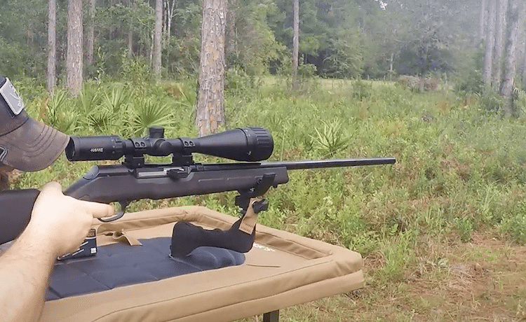 Man aiming a rifle with a scope in an outdoor setting