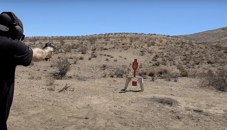 Man aiming a gun with a miniature rifle optic at a target