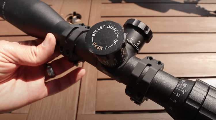 Hand holding a scope with scope rings and a wooden background